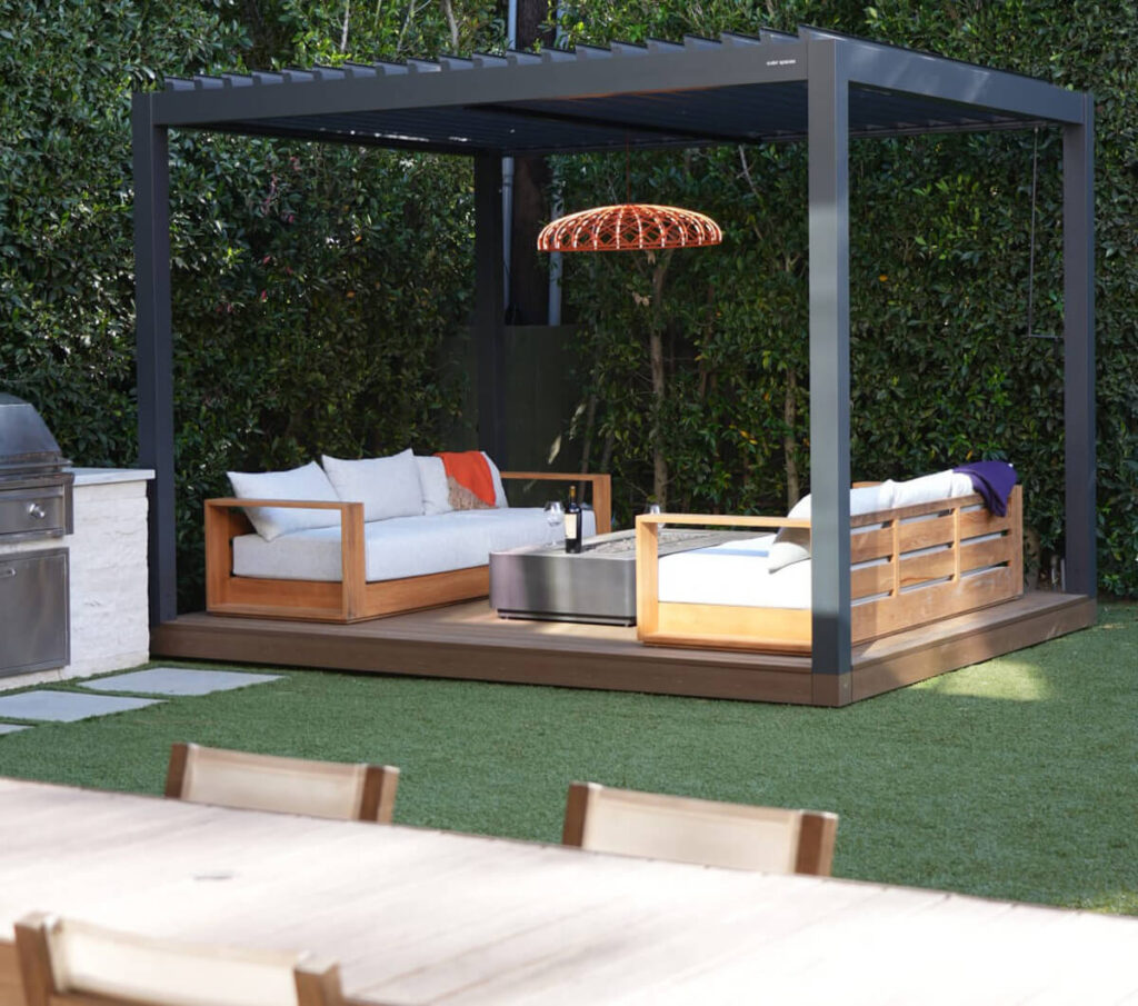 Join Us For A Live Build Demo With Outer Spaces &Amp; Designer Danny Wang 1 Modern backyard patio design featuring a dark louvered pergola over a wooden deck, artificial turf lawn, and lush privacy hedge background.